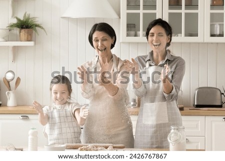 Multigenerational women, Hispanic woman her daughter and mature mom prepare homemade pastry, laugh, clap hands, spilling flour, enjoy cooking together, spend funny cookery in kitchen. Family pastime Royalty-Free Stock Photo #2426767867