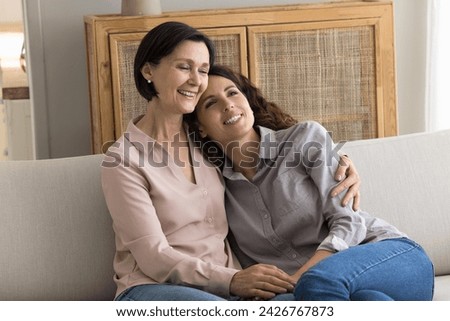 Happy young adult daughter enjoying priceless carefree time with mature mother, hugging seated on sofa at home, tell stories, having nostalgic mood, recollect memories, share news and plans at home Royalty-Free Stock Photo #2426767873