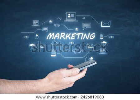 Hand holding a smartphone with MARKETING text and related icons on a virtual screen. Digital strategy concept