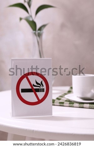 No Smoking sign and cup of coffee on white table indoors