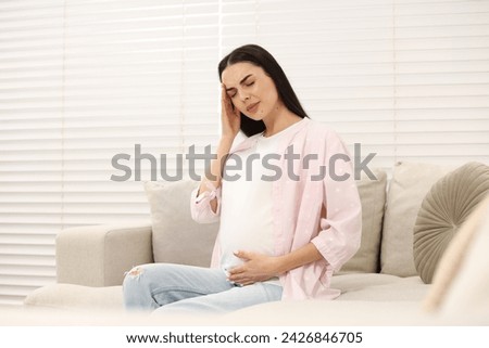 Pregnant woman suffering from headache on sofa at home Royalty-Free Stock Photo #2426846705