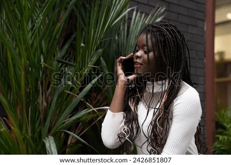 Portrait of beautiful young African American woman showing long black hair braided hairstyle and using mobile phone while feeling happy and smiling in the city outdoor