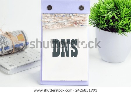 DNS. Domain Name System word writing on a desktop tear-off calendar on a white background, next to a calculator with a roll of banknotes with a flower out of focus in the background