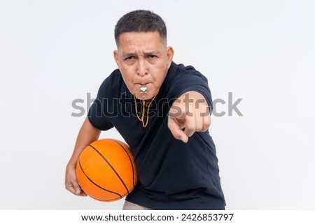 An irate middle-aged basketball coach or referee in casual attire holding a ball blowing a whistle, calling a foul. Isolated on a white background.