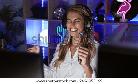 Vivacious young blonde woman streamer jubilantly wins at video game, live-streaming her victory from the buzzing gaming room at night Royalty-Free Stock Photo #2426855169