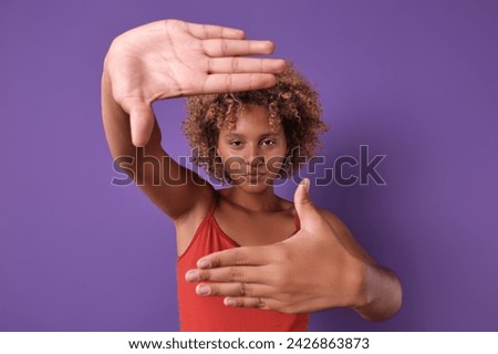 Young determined successful African American woman teenager selects good frame to start photo shoot to create model portfolio or portrait for business card website stands posing in purple studio.