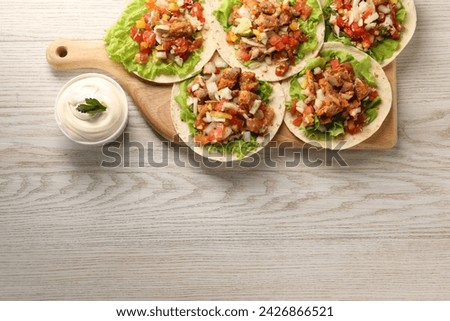 Delicious tacos with vegetables, meat and sauce on white wooden table, top view. Space for text