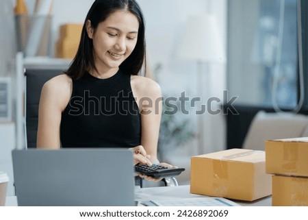 Entrepreneur using calculator with pencil in her hand, calculating financial expense at home office,online market packing box delivery,Startup successful small business owner, SME, concept.