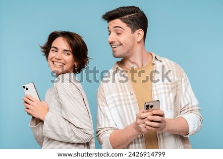 Curious man looking at smartphone of his girlfriend isolated on blue background. Happy friends holding mobile phones, communication online. Technology, social media addiction concept 