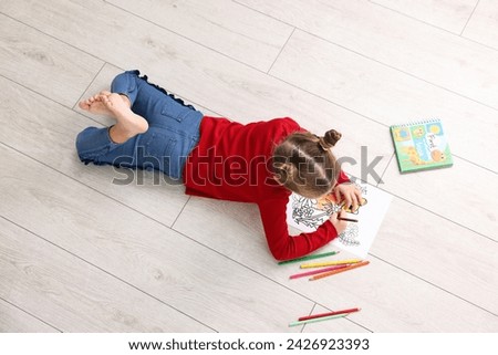 Cute little girl coloring on warm floor indoors, top view. Heating system