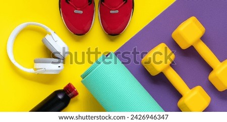 Dumbbells on purple roll mat on yellow background. Sport lifestyle concept. Flat lay. Red sneakers, music headphones, earphones and water bottle. Fitness equipment top view Royalty-Free Stock Photo #2426946347