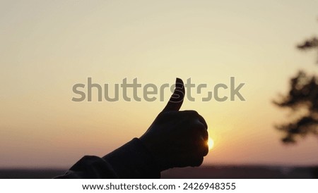 Gesture to show hand like outdoors, silhouette. Hand with raised thumb against background of sunset, sunrise with sun glare closeup. Approval, satisfaction, positive. Hand gesture class. Good symbol