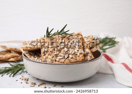 Cereal crackers with flax, sunflower, sesame seeds and rosemary in bowl on light table, closeup