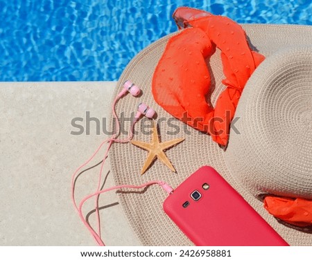 Women's raffia hat, telephone and starfish next to the pool against the backdrop of blue water.