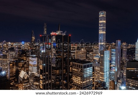 Night city scene with modern high rise buildings in metropolis. Dark glossy glass facade reflecting surrounding lights. Manhattan, New York City, USA