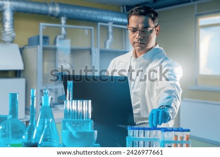 Man doctor in laboratory. Researcher with laptop and flasks. Table with test tubes near laboratory assistant. Scientist in industrial laboratory. Man corrects scientific experiment. Royalty-Free Stock Photo #2426977661