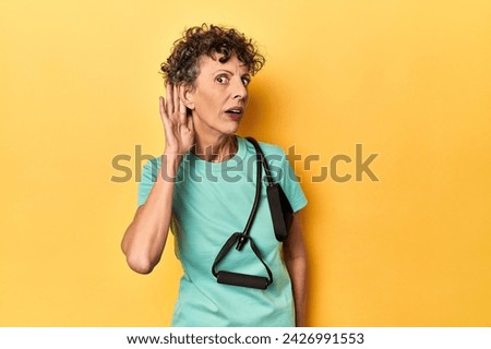 Sportswoman with resistance bands on yellow trying to listening a gossip. Royalty-Free Stock Photo #2426991553