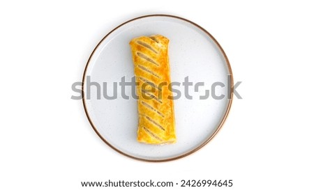 Overhead top down view of sausage roll Isolated on a plate. baked pastry with white background, no people and copy space. Golden yellow and brown pastry.