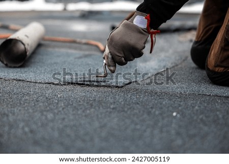 professional roofer applying bitumen roll on flat roof with a gas burner at a modern construction site Royalty-Free Stock Photo #2427005119