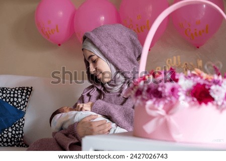 muslim arabic female celebrating with her newborn her birthday in living room with bouquet and balloons decorations in pink color