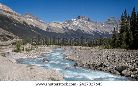 Glacial white water river with snow capped mountains in the background in Banff National Park in the Canadian Rockies, Royalty-Free Stock Photo #2427027645