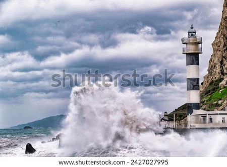 "Lighthouse amidst stormy sea, waves crashing, cloudy sky overhead."