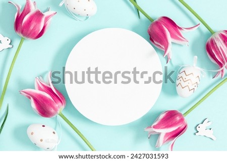 Easter decorations concept. Top view on empty circle, purple tulips flowers, colorful eggs on pastel blue background. Flat lay, top view, copy space