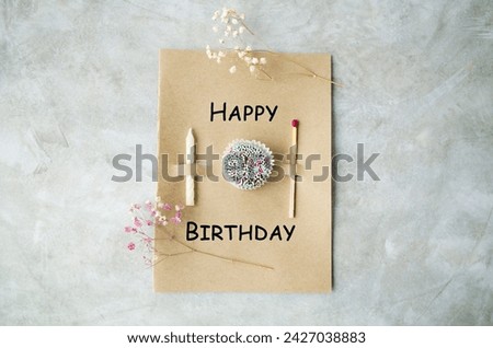 Handmade greeting card for your birthday.  A candle for a cake, a large match and a mini cake on craft paper and delicate flowers.  Paper craft concept.  Flat lay, top view.