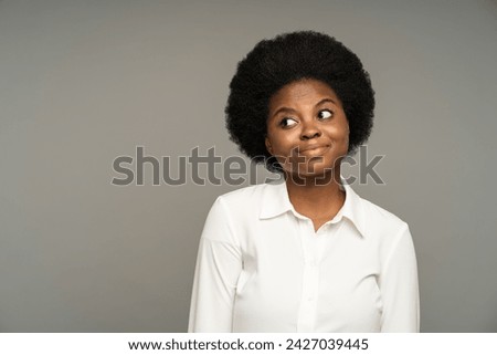 Thoughtful uncertain african american female with expression of doubt, hesitation on face. Confused pensive black female thinking of answer to hardball question isolated on grey studio background. Royalty-Free Stock Photo #2427039445