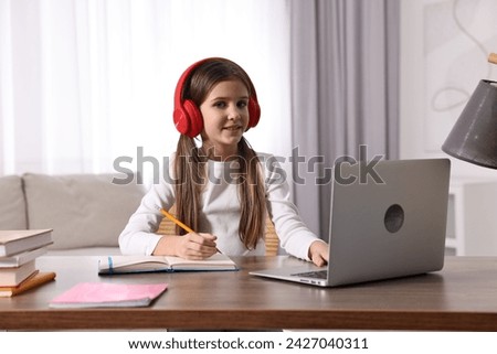 E-learning. Cute girl taking notes during online lesson at table indoors