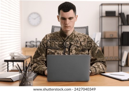 Military service. Young soldier working with laptop at wooden table in office