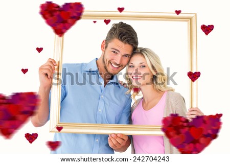 Attractive young couple holding picture frame against hearts