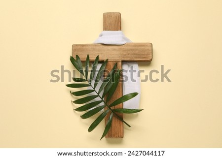 Wooden cross, white cloth and palm leaf on beige background, top view. Easter attributes Royalty-Free Stock Photo #2427044117