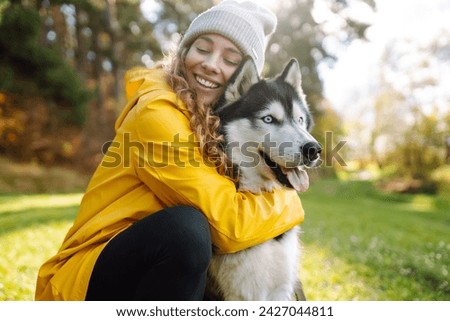 Beautiful young woman in a yellow coat walks in a park with her pet husky. A pet owner spends time with her dog. Concept of fun, entertainment. Royalty-Free Stock Photo #2427044811