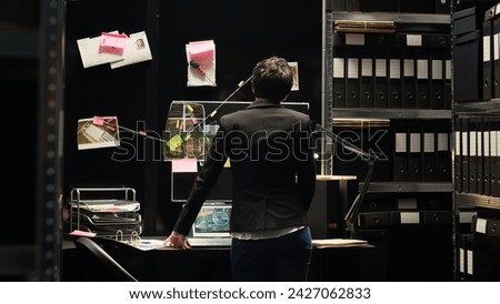 Police inspector reviewing proof hanged on board in incident room, using criminal expertise and forensic science to uncover clues. Detective gathering intelligence to solve case. Tripod shot. Royalty-Free Stock Photo #2427062833
