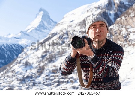 Traveler with passion for photography enjoying hiking in Swiss Alps in wintertime, taking pictures of nature with professional camera