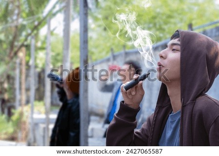 Asian male teenager is smoking electronic cigarette or vapor and drinking alcohol with friends in secret area, soft focus, daily life problems and bad habit and behavior of teenagers concept.