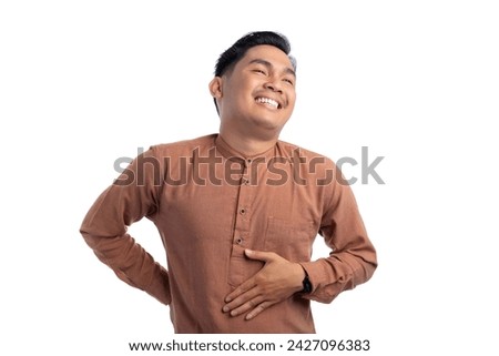 Happy Asian Muslim man touching his stomach feeling full after delicious meal with relieved expression isolated on white background. Ramadan and Eid Fitr celebration concept Royalty-Free Stock Photo #2427096383