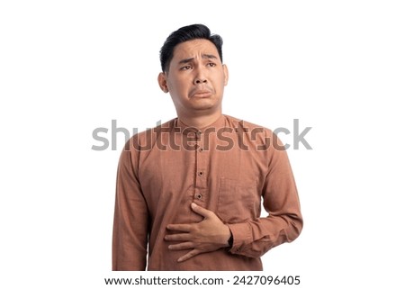 Handsome Asian Muslim man touching his stomach feels hungry and wants to eat delicious food isolated on white background. Ramadan and Eid Fitr celebration concept Royalty-Free Stock Photo #2427096405