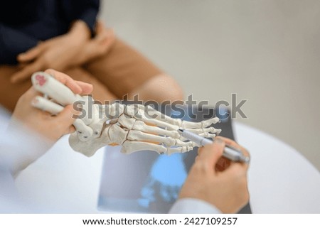 A orthopedic doctor points to a model of ankle and foot bones explaining to a patient a foot bone problem. Health care and spine concept