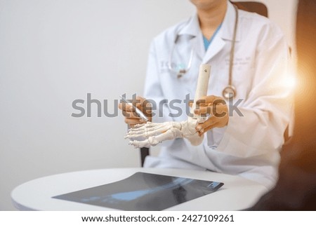 An orthopedic doctor points to a model of ankle and foot bones explaining to a patient a foot bone problem. Health care and spine concept
