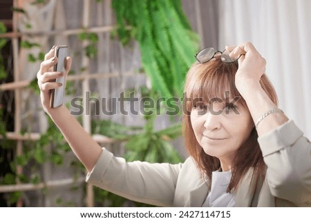 An elderly senior woman with a cell phone takes a selfie. A lady blogger is chatting online. Technologies for pensioners