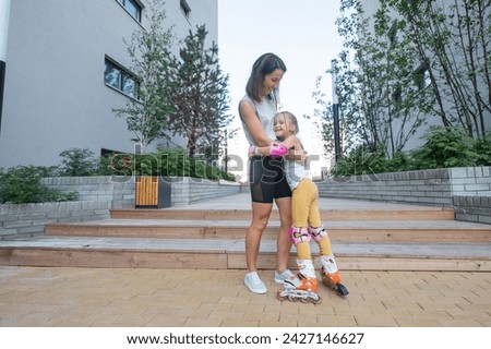 Mother helps daughter learn to roller skate. 