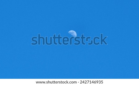 This is a picture of the moon the day. The blue sky and the white moon contrast