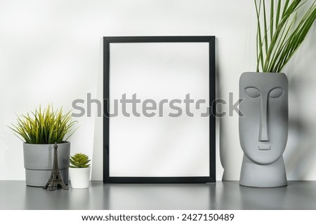 Black wooden frame and gray vase with plant leaves against white wall