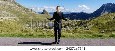 Panoramic photo of a man training against the background of mountains. An athlete jumps on a rope.