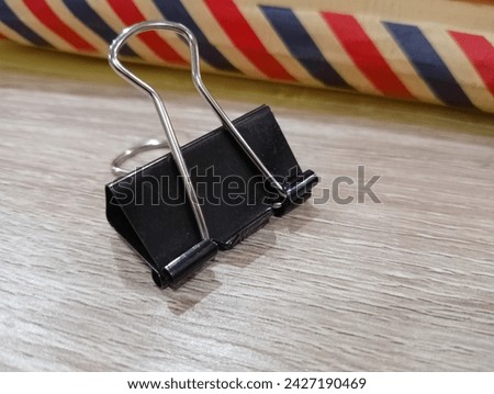 A paper clip made of metal placed on a wooden patterned table and next to a brown letter envelope