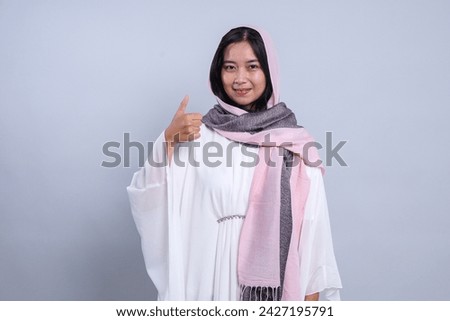 Asian Muslim woman wearing a headscarf gives thumbs up hand gesture of approval