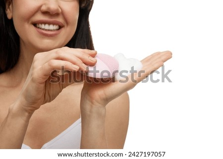 Close-up portrait of of woman holding pink facial cleansing brush with foam against white studio background. Concept of beauty and self care, wellness, skincare, hygiene procedures. Royalty-Free Stock Photo #2427197057
