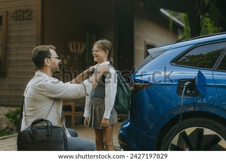 Portrait of a man charging electric car in front of his house.Man is unplugging charger from the fully charged car before driving daughter to school. Royalty-Free Stock Photo #2427197829